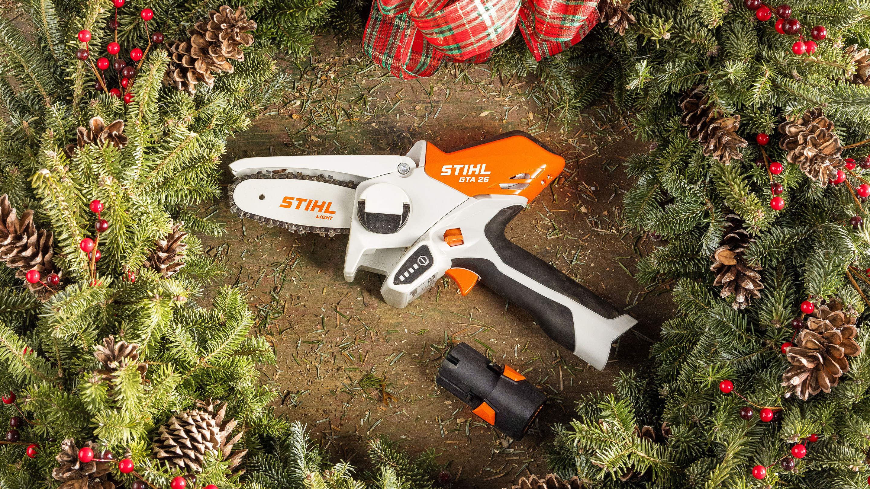 STIHL GTA 26 dans une couronne de l’Avent, entourée de vert sapin, de pommes de pin et d’un ruban