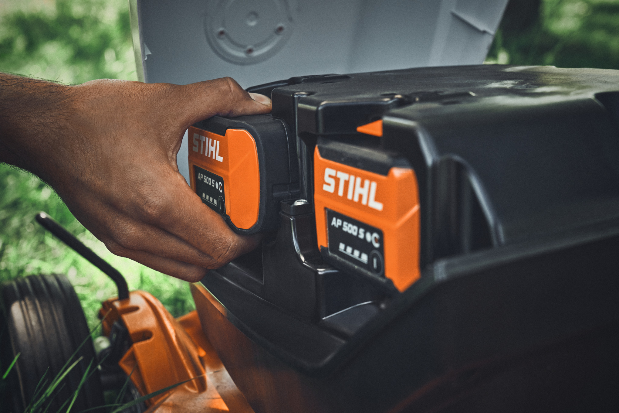 Une personne branche une batterie STIHL AP 500 S dans une tondeuse à gazon sans fil STIHL.