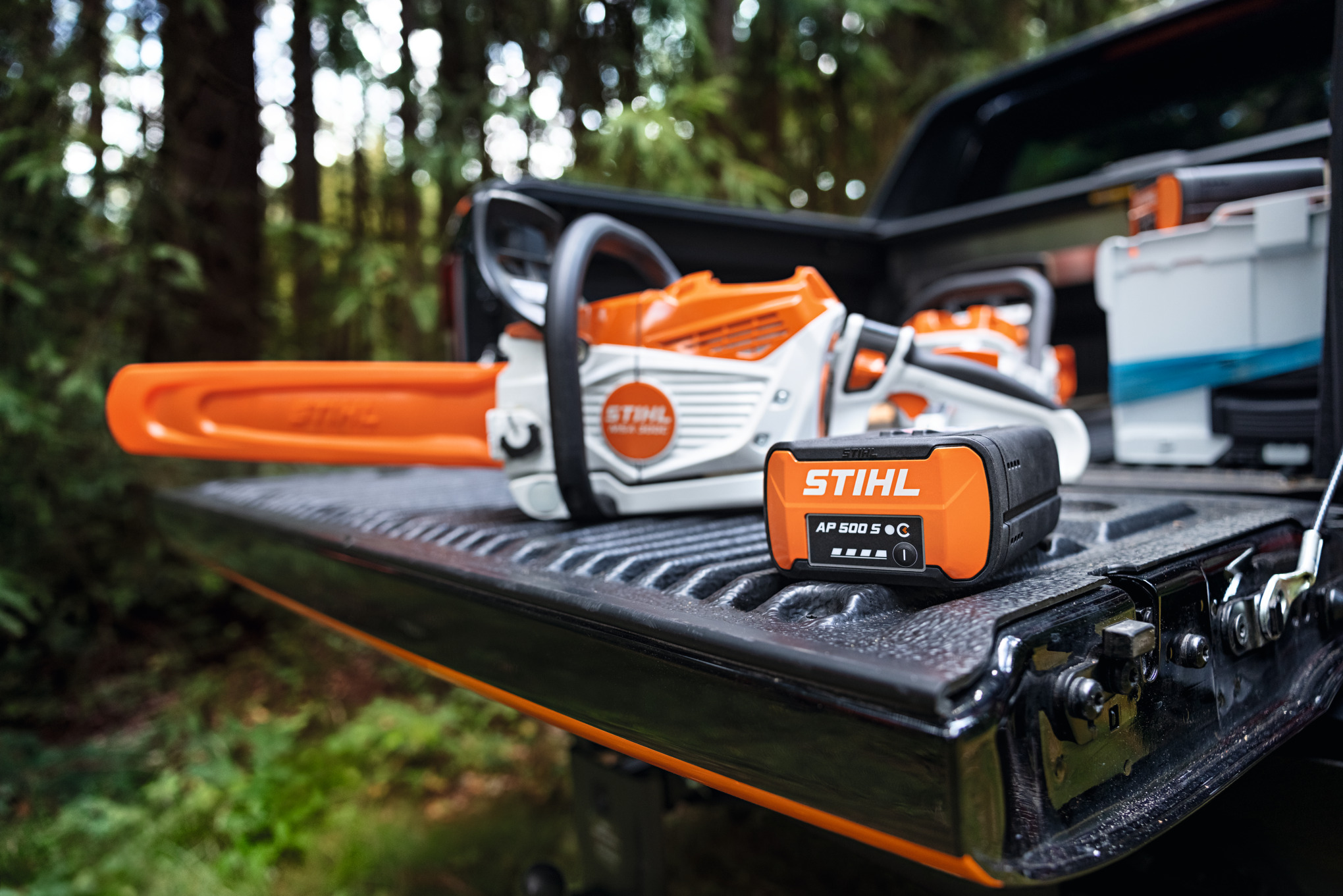 Une batterie AP 500 S et une tronçonneuse à batterie à l'arriere d'un pick up dans une forêt